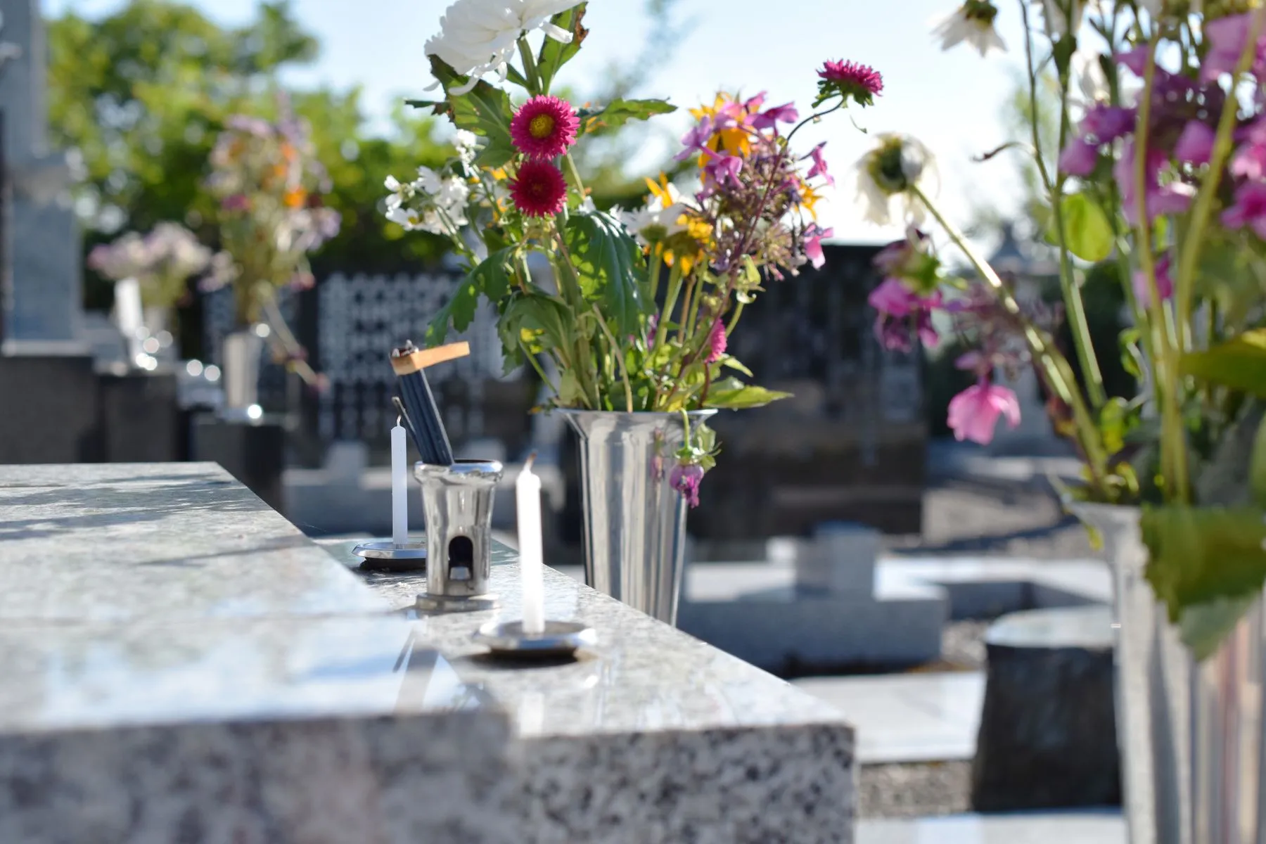 Vase de fleurs et petites bougies posés sur une pierre tombale en granit rénovée
