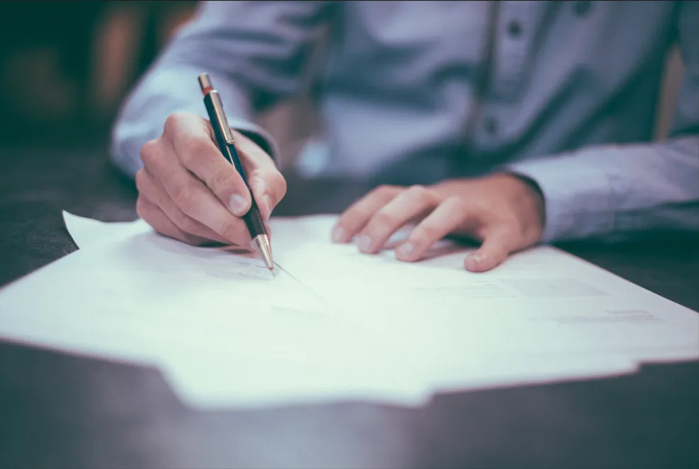 Gros plan sur les mains d'une personne remplissant des documents administratifs pour l'accompagnement des familles.